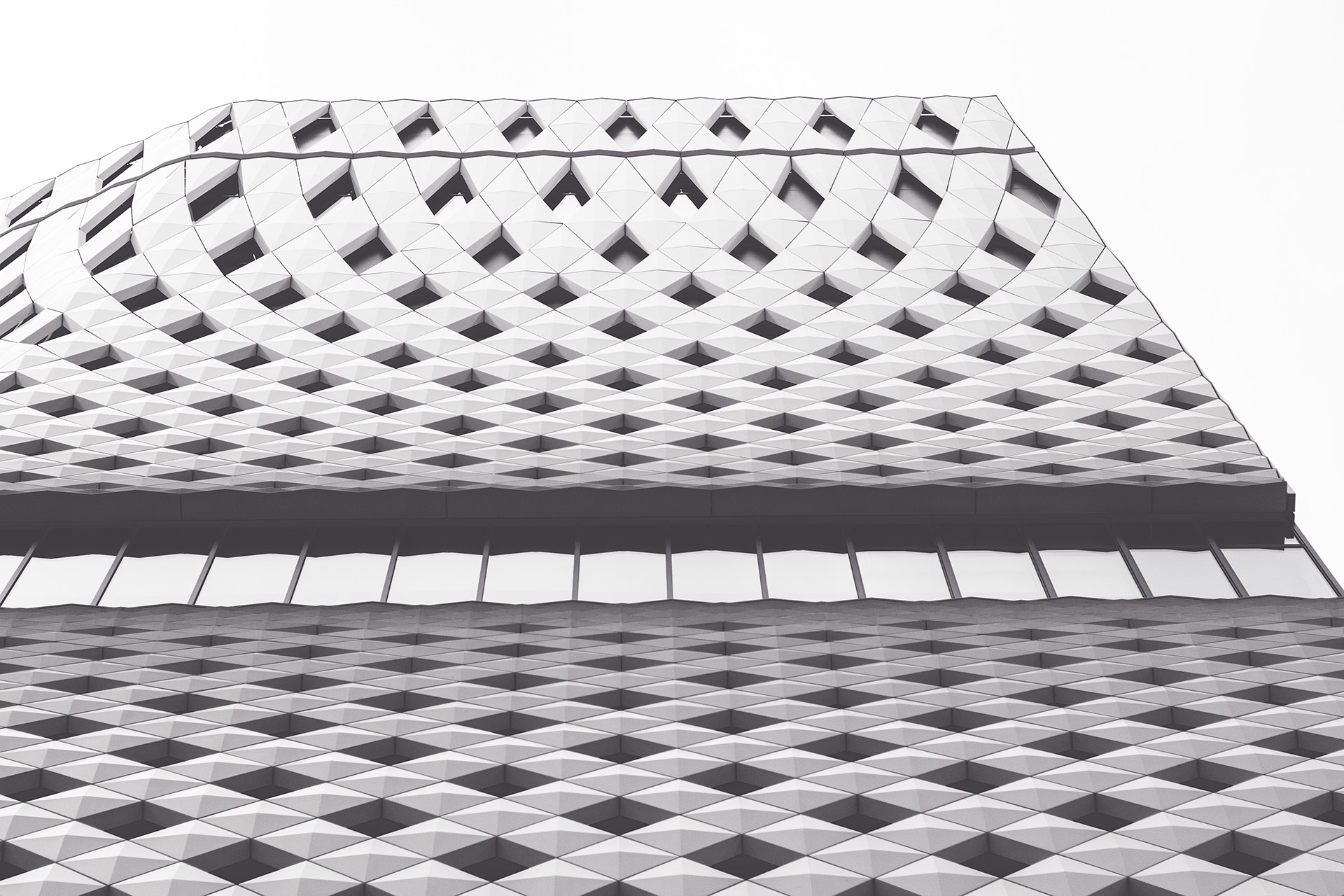 Pale facade of a contemporary building featuring a geometric criss-cross wave pattern pinching at the center near its windows.